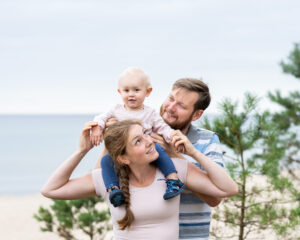 Lekfull familjefotografering på stranden i Åhus nära Kristianstad flicka rider på mammas axlar