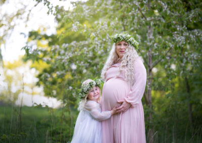 Utomhus gravidfotografering på våren med dotter i lånad klänning och kransar i Kristianstad nära Lund och Hässleholm