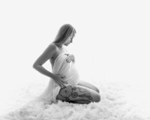 Hudnära gravidfotografering Johanna sittande med draperat tyg med vit bakgrund i studio i Kristianstad nära Hässleholm