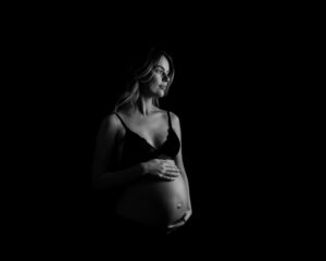 Hudnära Gravidfotografering i Kristianstad nära Sölvesborg och Bromölla Mimmi med bar mage och mycket skuggor och svart bakgrund