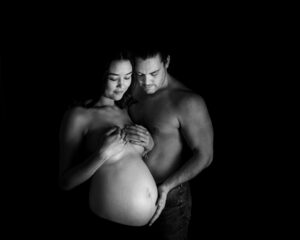 Hudnära gravidfotografering Jennifer med partner med bar mage och mycket skuggor i studio i Kristianstad nära Lund och Hörby