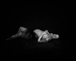 Hudnära gravidfotografering med mycket skuggor Matilda liggande draperad i tyg i studio i Kristianstad nära Lund och Hässleholm