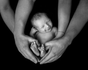 Nyföddfotografering bebis som ler i föräldranas i händer i studion i Kristianstad nära Hässleholm